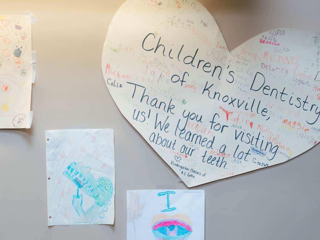 Large heart-shaped poster on a wall reads "Children's Dentistry of Knoxville" with thanks and drawings, illustrating a dental visit experience.