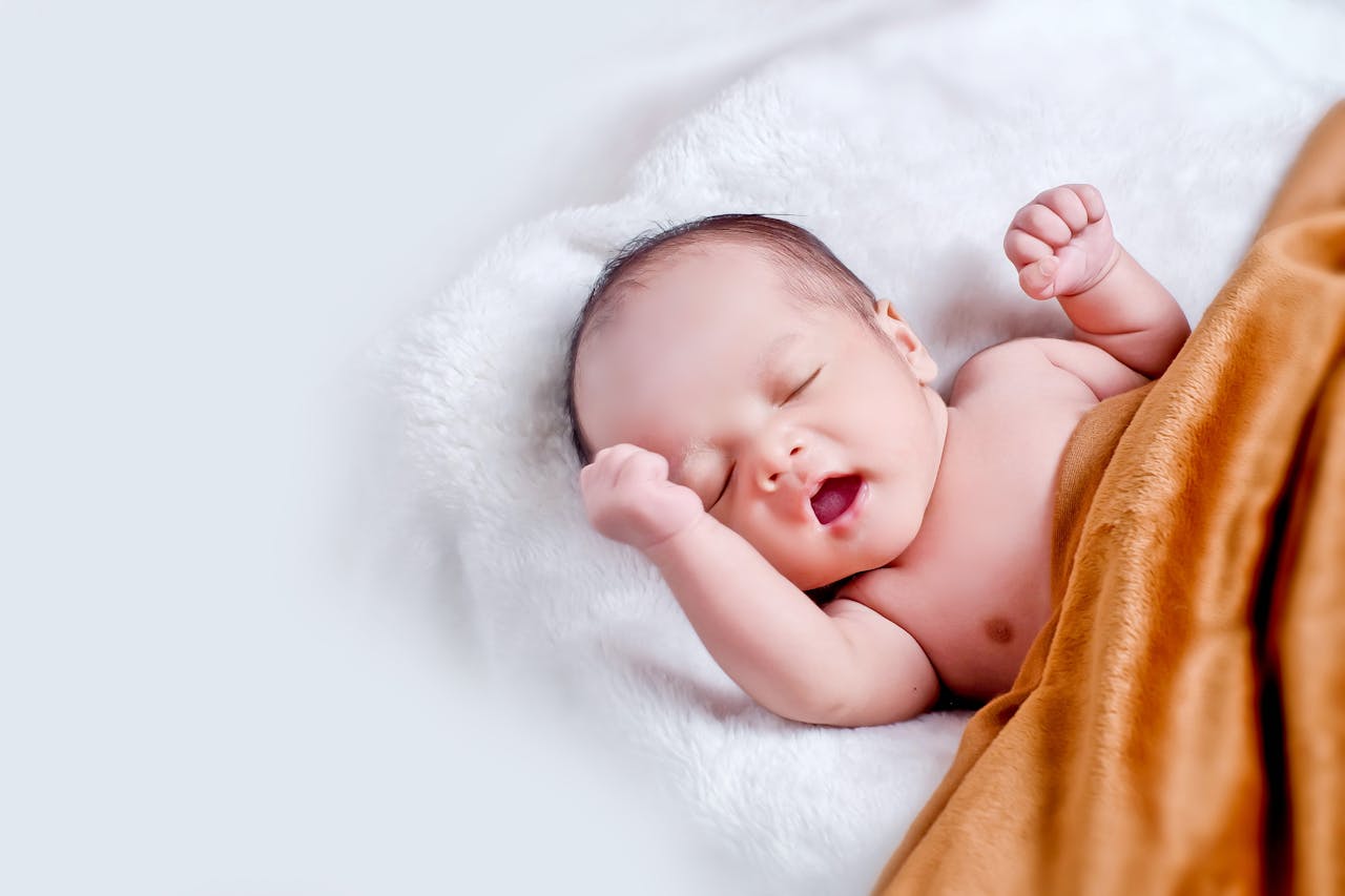 A newborn baby sleeps peacefully, wrapped in a soft, brown blanket on a fluffy, white surface, basking in gentle, diffused lighting.