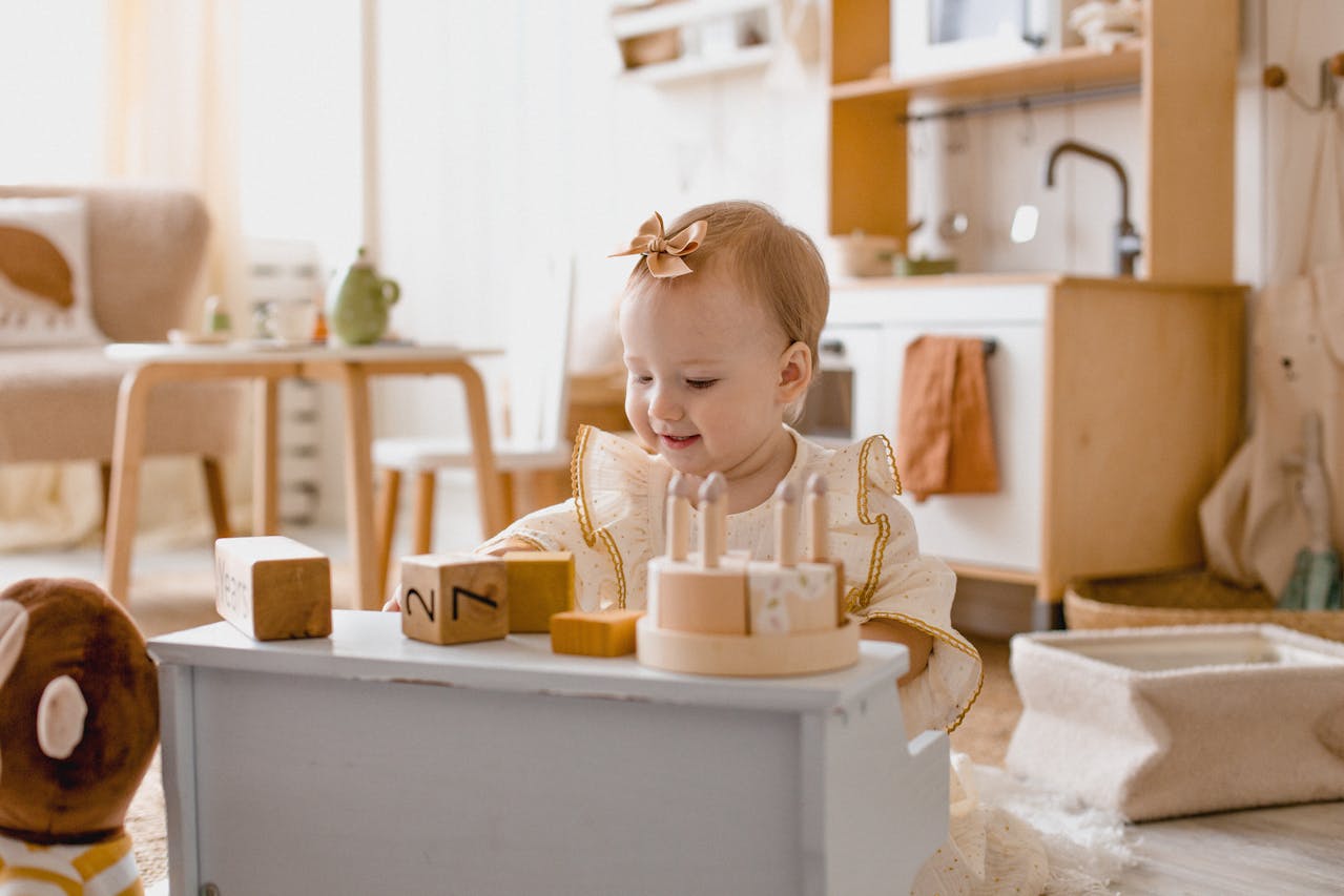 A child happily plays with wooden blocks at a small play table in a cozy, sunlit room with soft, neutral decor.